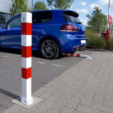 Wit-rode neerklapbare afzetpaal 70x70 mm met betonvoet, staand en neergeklapt bij een parkeerplaats.
