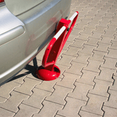 Rood-witte parkeerbeugel met cilinderslot, opklapbaar, naast een zilveren auto op grijze tegels.