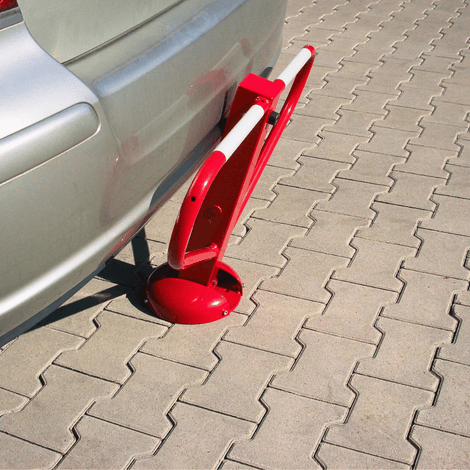 Rood-witte parkeerbeugel met cilinderslot, opklapbaar, naast een zilveren auto op grijze tegels.