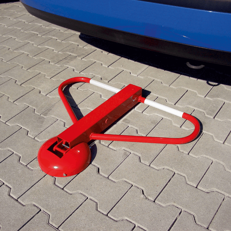 Rood-witte parkeerbeugel met cilinderslot, plat op grijze tegels voor een blauwe auto.