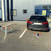 Wit-rode parkeerbeugel in open en gesloten positie op asfalt, met zwarte auto op parkeerplaats.