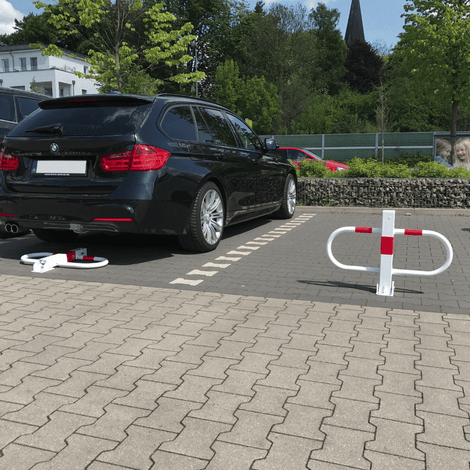 Witte en rode parkeerbeugel, neergeklapt naast een zwarte auto, met een staande beugel ernaast.
