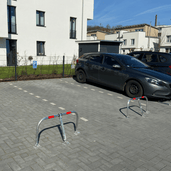 Verzinkt stalen parkeerbeugels met rode reflectie, geplaatst op een parkeerplaats met een grijze auto.