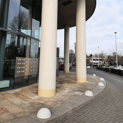Grijze betonnen parkeerbol Ø400 mm zonder voet, langs een gebouw met glazen gevel.