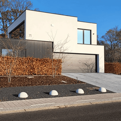 Vier grijze betonnen parkeerbollen (Ø500 mm) zonder voet, langs een oprit bij een moderne woning.