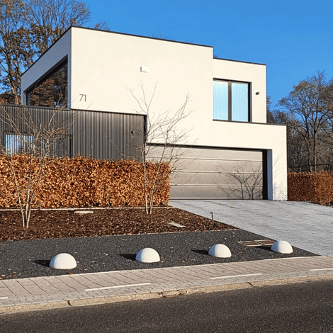Vier grijze betonnen parkeerbollen (Ø500 mm) zonder voet, langs een oprit bij een moderne woning.