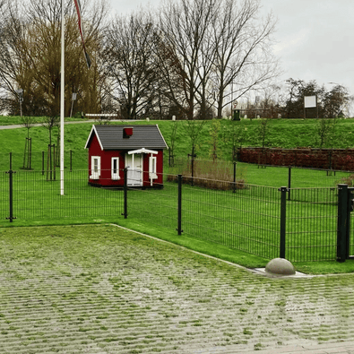 Grijze betonnen parkeerbol op voet, Ø350 mm, naast een groen gazon en een rood huisje.