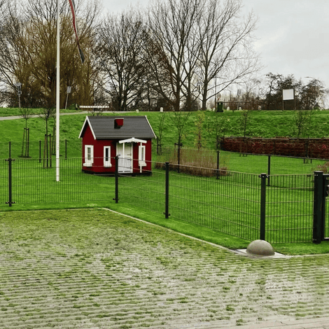 Grijze betonnen parkeerbol op voet, Ø350 mm, naast een groen gazon en een rood huisje.