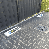 Witte stootbanden met blauw-geel "P DIE-SIGN" logo op een grijze klinkerparkeerplaats.