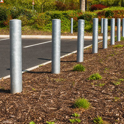 Ronde parkeerpalen van verzinkt staal, Ø102 mm, geplaatst langs een parkeerplaats met boomschors.