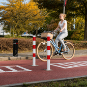 Witte en rood gestreepte parkeerpaal Ø89 mm op een fietspad, met een fietser op de achtergrond.