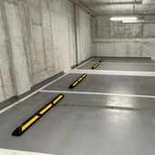 Zwarte rubberen parkeerstop van 120 cm met gele 3M reflectoren in een parkeergarage.