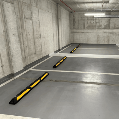 Zwarte rubberen parkeerstop van 120 cm met gele 3M reflectoren in een parkeergarage.