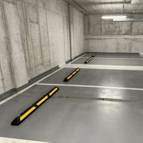 Zwarte rubberen parkeerstop van 120 cm met gele 3M reflectoren in een parkeergarage.