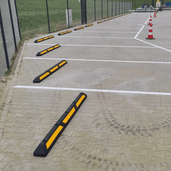 Zwarte rubberen parkeerstop met gele 3M reflectoren op een parkeerplaats.
