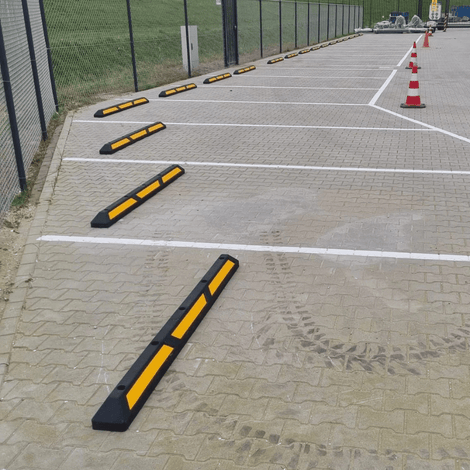 Zwarte rubberen parkeerstop met gele 3M reflectoren op een parkeerplaats.