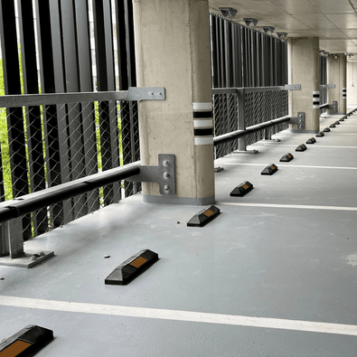 Zwarte rubberen parkeerstops met oranje reflectoren in een parkeergarage.
