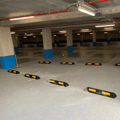 Zwarte rubberen parkeerstop van 90 cm met gele 3M reflectoren in een parkeergarage.