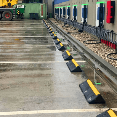 Zwarte rubberen wielstops met gele 3M reflectoren op een natte parkeerplaats bij laadpalen.