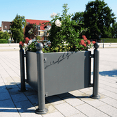 Antraciet verzinkt stalen plantenbak (88x88x68 cm) met ornamenten en bloemen op een plein.