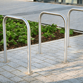 Drie RVS fietsbeugels (Ø48 mm) met betonvoeten op grijze tegels, naast een groen perk.