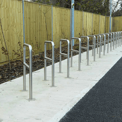 RVS fietsbeugels met tussenbuis en betonvoeten, Ø48 mm, in een rij op een betonnen ondergrond.