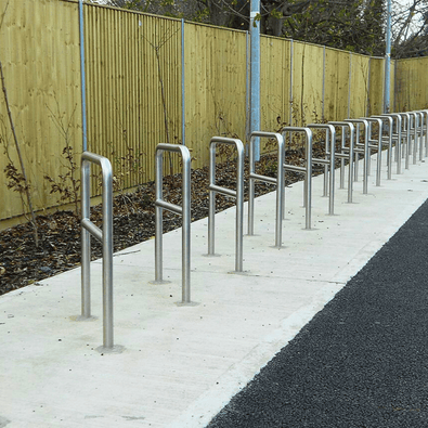 RVS fietsbeugels Ø48 mm, verankerd in beton, met tussenbuis, op een rij langs een pad.