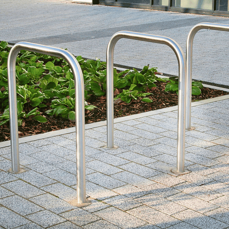 RVS fietsbeugel Ø48 mm, voor verankering in beton, zonder tussenbuis, op grijze tegels met groen.