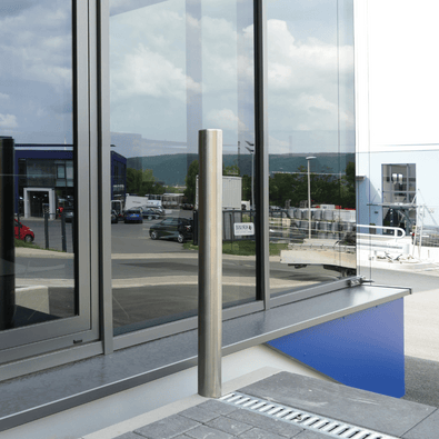 RVS parkeerpaal Ø76 mm, geborsteld, voor verankering in beton, naast een modern gebouw.