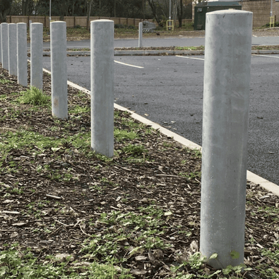 Zeven grijze, ronde Rampaal Ø152 mm van verzinkt staal, geplaatst langs een parkeerplaats.