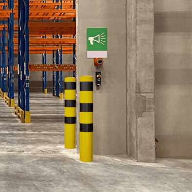 Twee gele en zwarte Ø193 mm rampaalen voor betonverankering in een magazijn.
