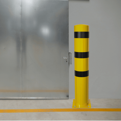 Gele en zwarte rampaal Ø273 mm op voetplaat, staand voor een metalen deur.