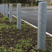 Zeven rampalen Ø152 mm van verzinkt staal, geplaatst langs een parkeerplaats