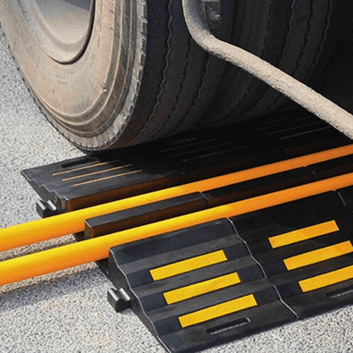 Zwarte rubberen slangenbrug met 2 kanalen en gele strepen, beschermt kabels onder een vrachtwagenwiel.