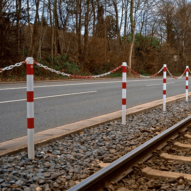 Witte en rood gestreepte kettingpalen Ø60 mm met kettingen langs een weg en spoorlijn.