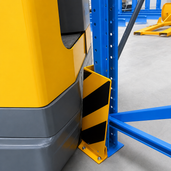 Geel-zwart flexibel hoekprofiel stootbeschermer voor vloermontage, beschermt een blauw magazijnrek tegen een gele heftruck.