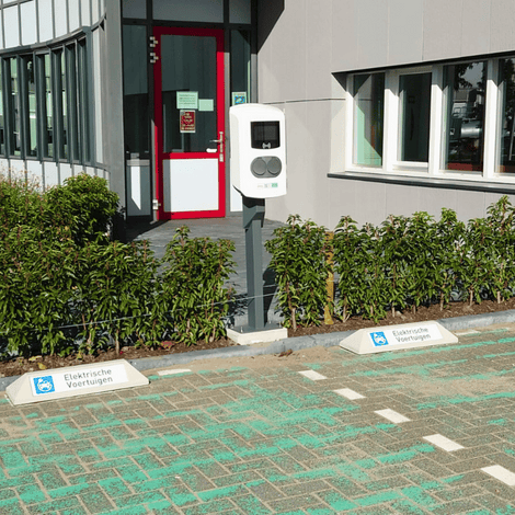 Witte betonnen stootbanden met blauw "Elektrische Voertuigen" logo bij een laadpaal.