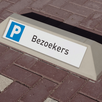 Grijze betonnen stootband met "Bezoekers" tekst en blauw P-symbool op een parkeerplaats.