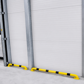 Gele en zwart gestreepte stootbeschermer Ø60 mm op voetplaat, gemonteerd voor een witte garagedeur.