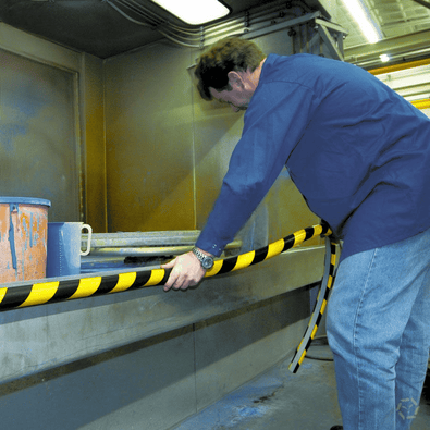 Zelfklevende geel-zwarte stootbescherming profielen, gemonteerd door een man in een industriële omgeving.