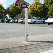 Uitneembare RVS afzetpaal Ø102 mm met betonvoet en slot, glanzend zilver, in een parkeerplaats.