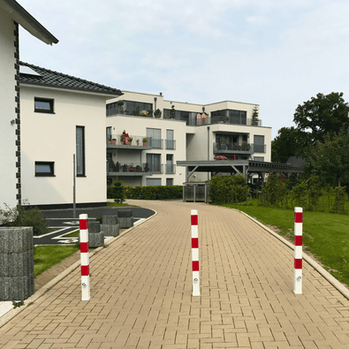 Drie wit-rode, uitneembare afzetpalen van 70x70 mm met betonvoet op een oprit.