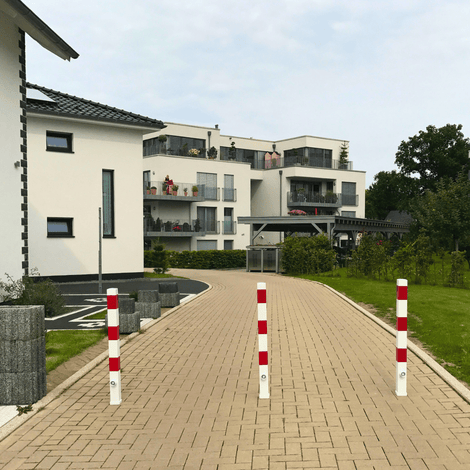 Drie wit-rode, uitneembare afzetpalen van 70x70 mm met betonvoet op een oprit.