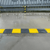 Zwarte en gele verkeersdrempel van 3 cm hoog op nat asfalt, met reflecterende strepen.