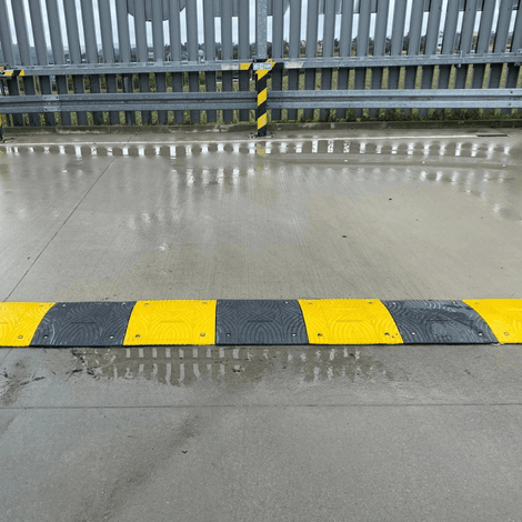 Zwarte en gele verkeersdrempel van 3 cm hoog op nat asfalt, met reflecterende strepen.