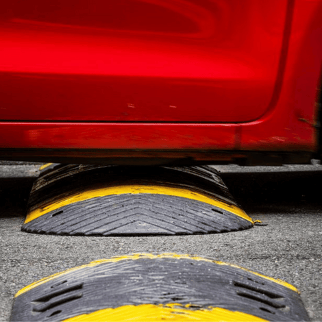 Zwarte rubberen verkeersdrempel met gele strepen, 7 cm hoog, onder een rode auto.