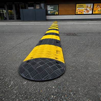 Zwarte en gele rubberen verkeersdrempel van 5 cm hoog op een asfalt weg bij Mc Donalds
