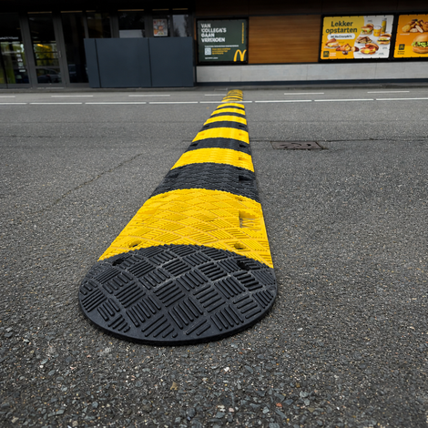 Zwarte en gele rubberen verkeersdrempel van 5 cm hoog op een asfalt weg bij Mc Donalds