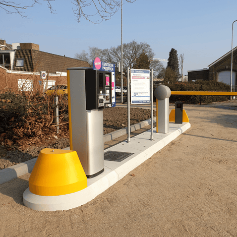 Prefab modulair verkeerseiland met grijze betaalautomaat, slagboom en gele kegel.
