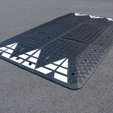 Zwart rubber verkeerskussen 300x180x6,5 cm met witte reflecterende pijlen en bevestigingsgaten.